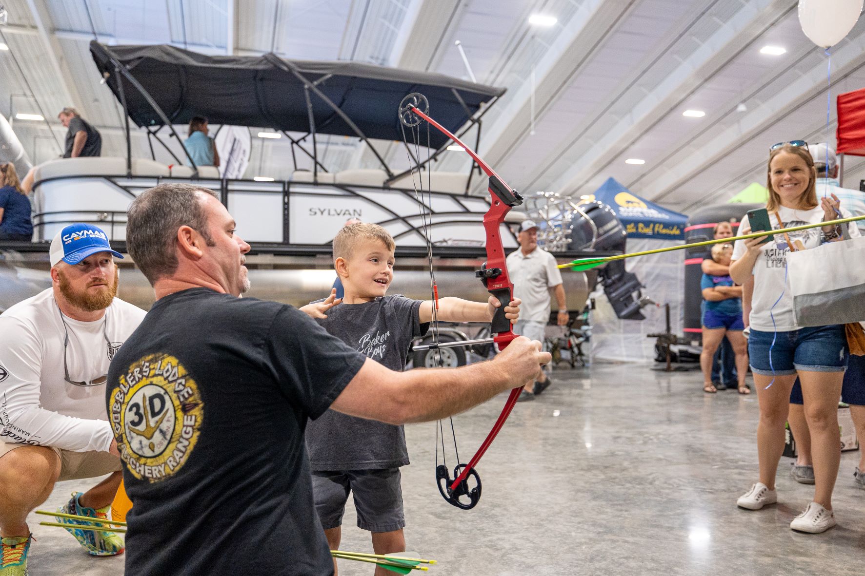 A staff member assists a young boy with his archery grip. 