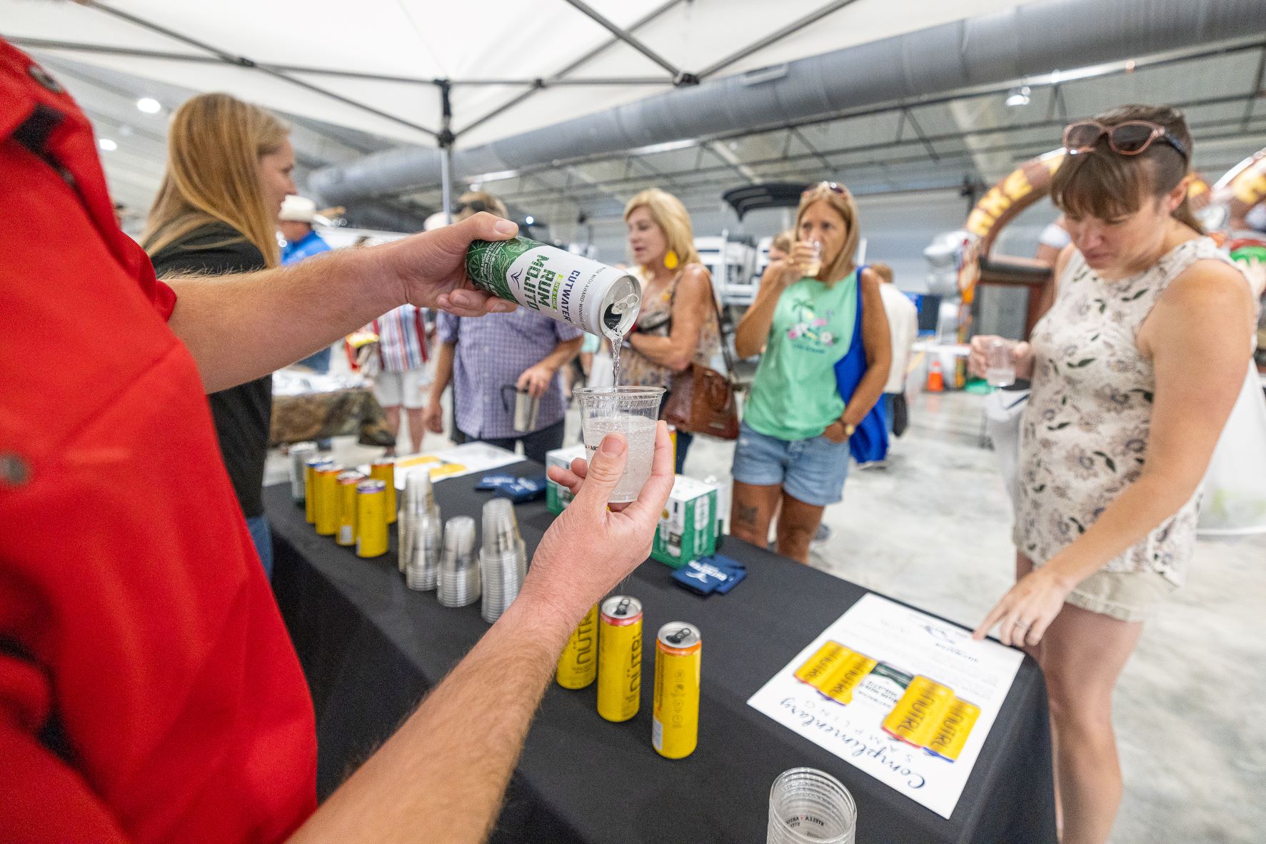 Man pours Cutwater Seltzer for women sampling beverages at event. Additional adult beverages are on table available for sampling. 